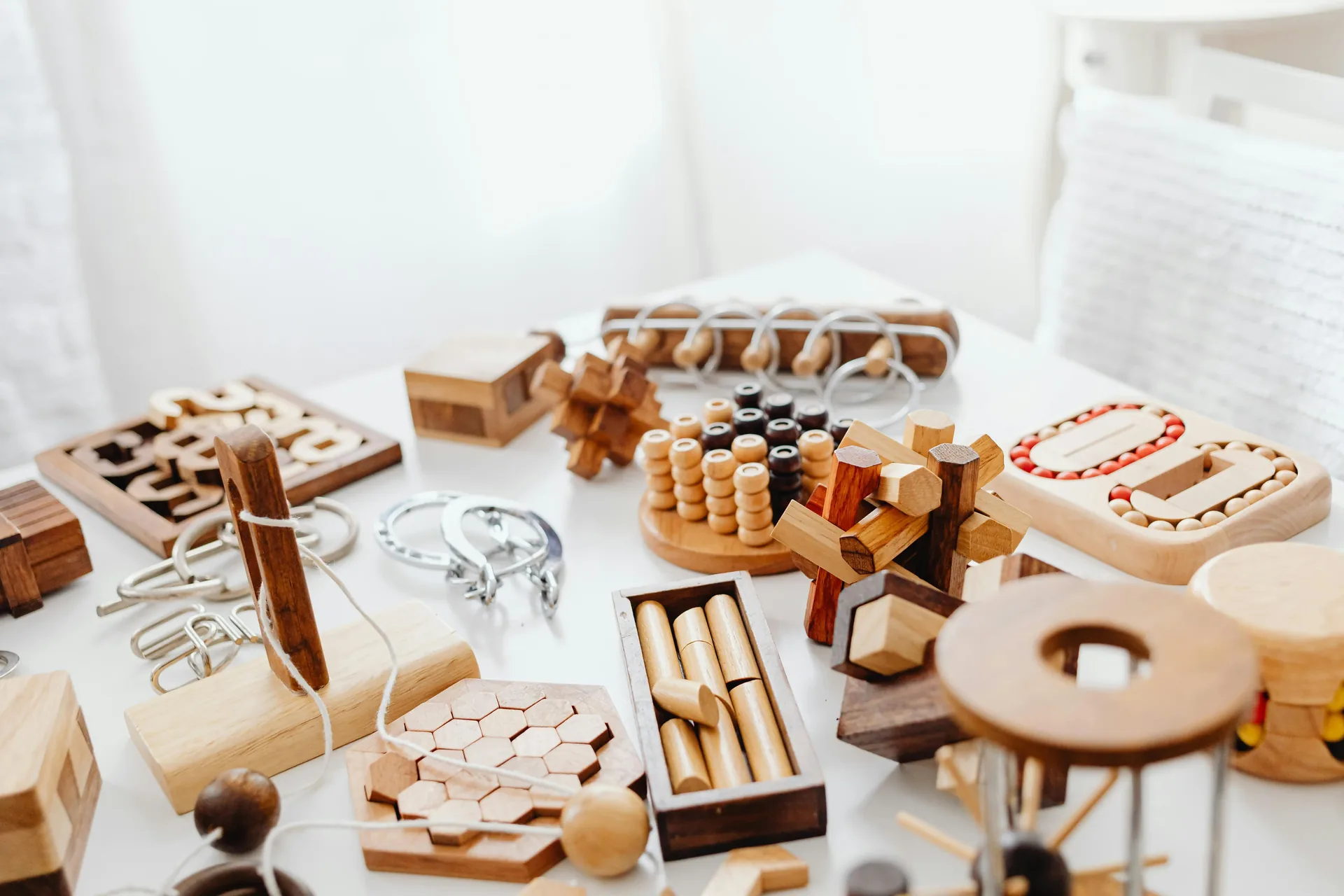 Collection of handcrafted wooden brain teaser puzzles and disentanglement puzzles arranged on a white surface
