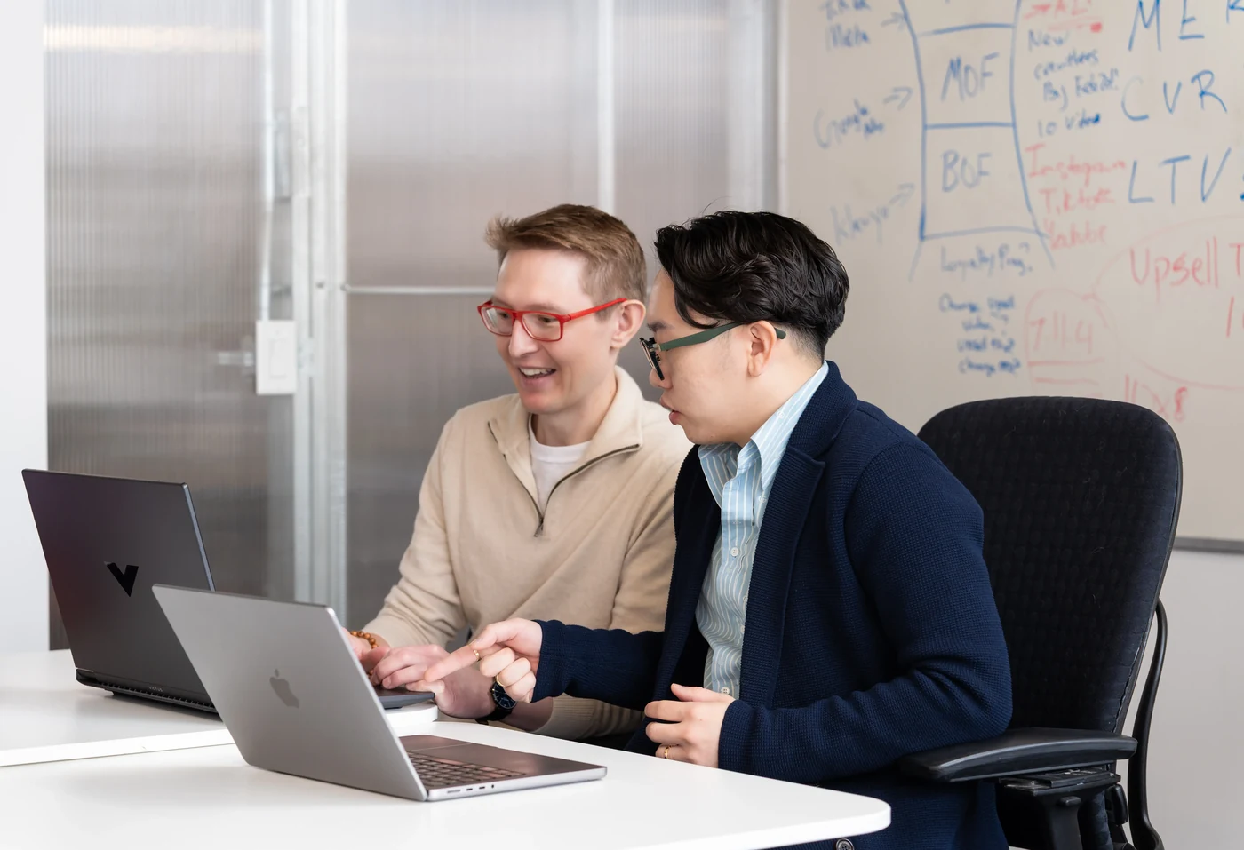 Two Navora strategists collaborating on laptops in front of a growth-metrics whiteboard